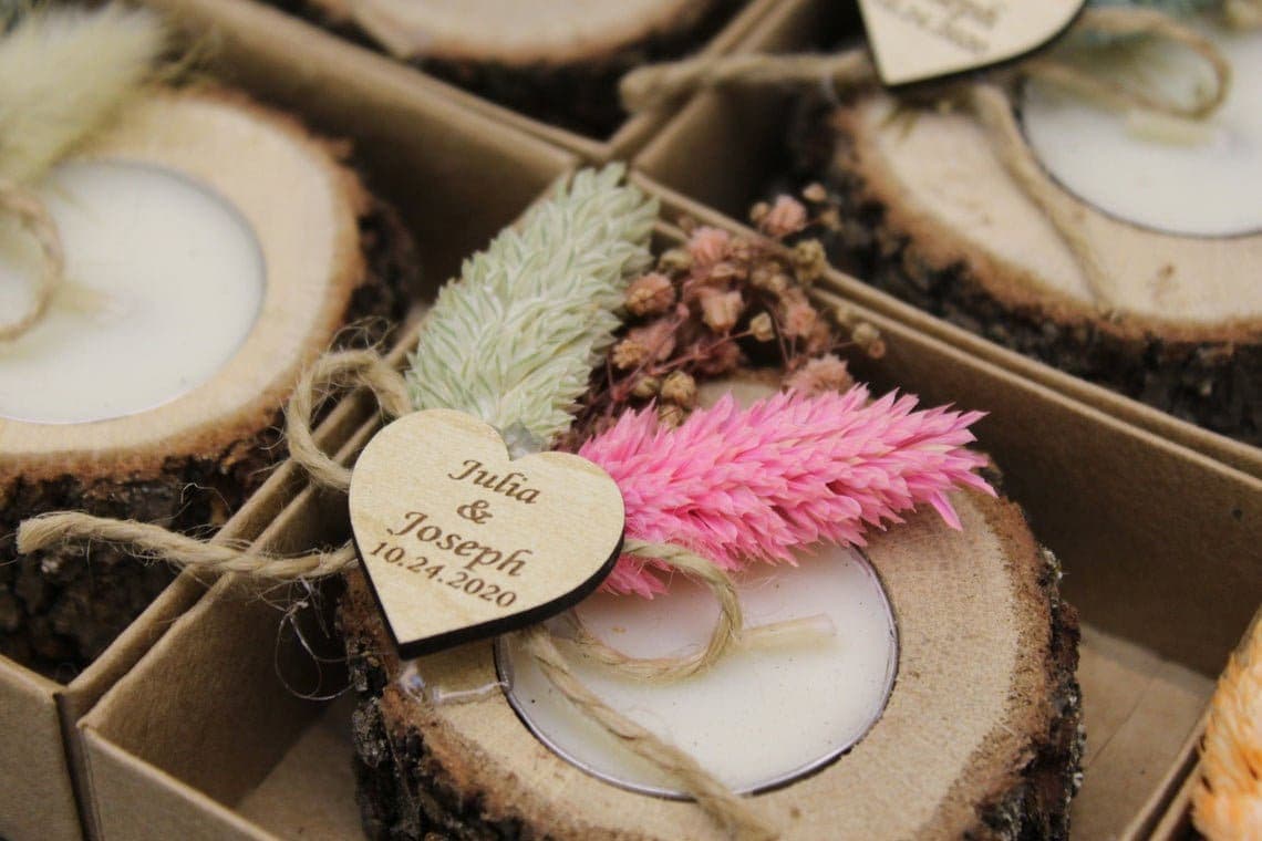 Rustic wooden candle holders with pink and green dried flowers and a heart tag reading Julia and Joseph with their wedding date