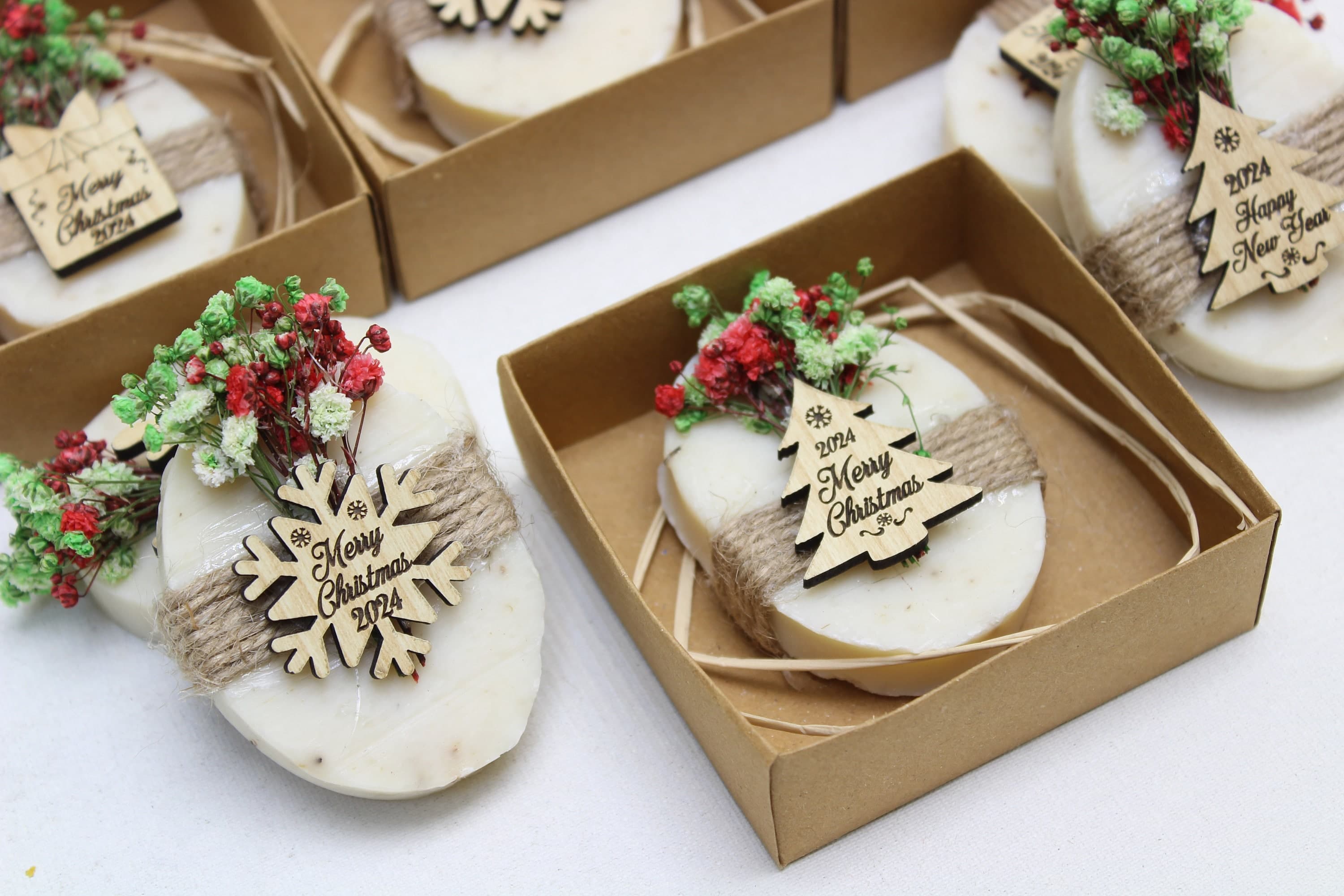 Oval soaps wrapped in twine with dried flowers and wooden Merry Christmas 2024 tags in small kraft boxes