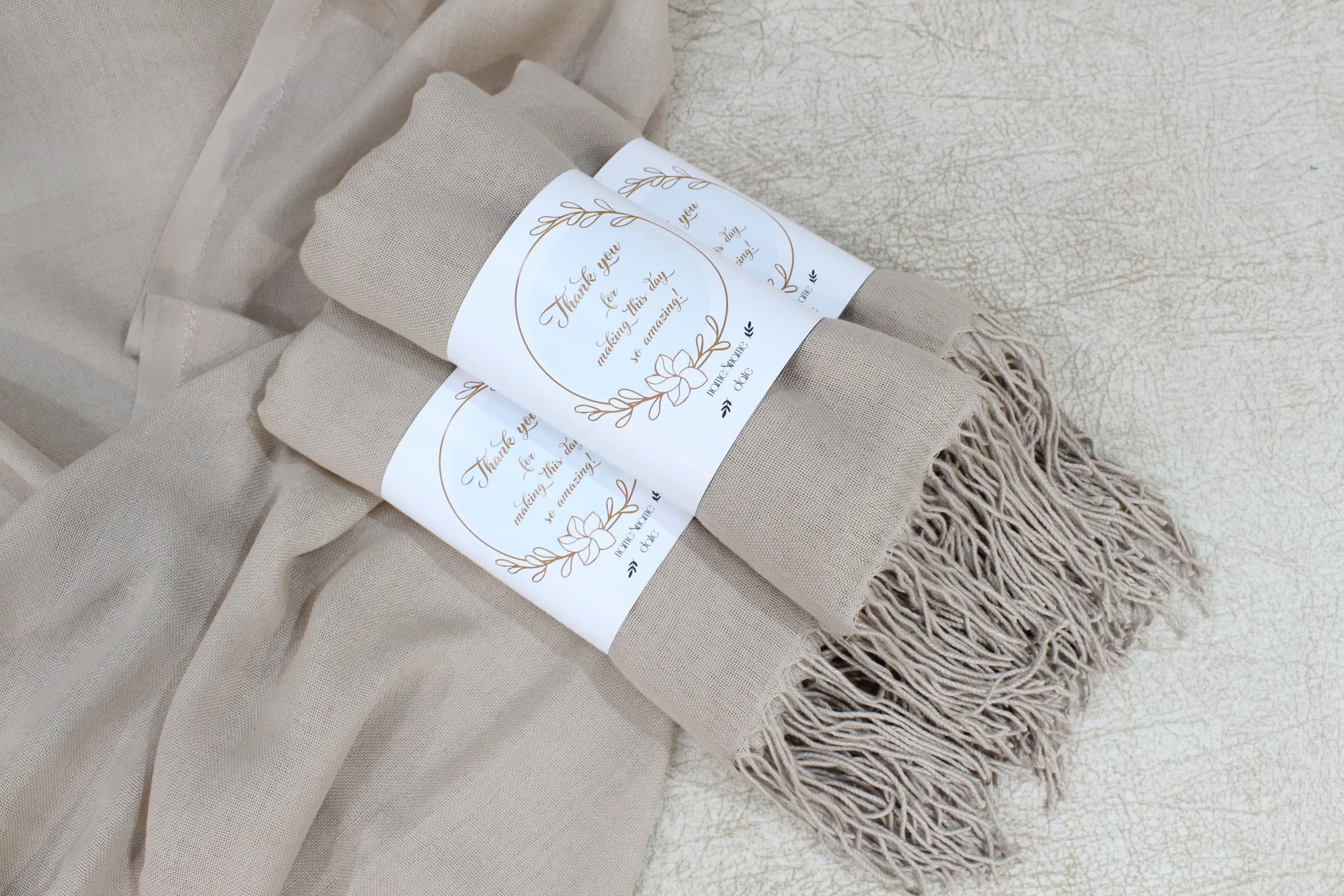 Two beige fringed pashmina shawls tied with white tags printed in gold with a thank you message